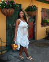 Woman in a white dress standing in front of a yellow building with hanging plants.