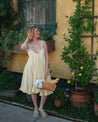 Woman in a yellow dress standing in front of a rustic building with plants.