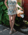 Woman in floral outfit holding a basket outdoors near a red door