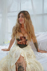 Woman sitting on a bed wearing a corset with a tattoo design, surrounded by white curtains.