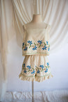 Beige top and shorts set with floral embroidery on a mannequin against a white curtain background. Upcycled Summer Fashion. Vintage Tablecloth