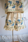 Beige shorts with floral embroidery on a mannequin, with measurements written on it.
