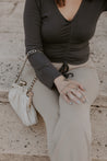 Woman sitting wearing charcoal cinch top sand color pants and holding purse