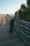 woman wearing blue cinch top and charcoal flare pant standing on wooden walkway