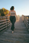 woman wearing sand color top with flare pant on wooden walkway 